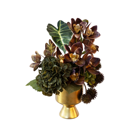 An artificial floral arrangement featuring dark burgundy orchids, green hydrangea blooms, and textured green foliage, presented in a metallic gold pedestal vase against a solid white background.
